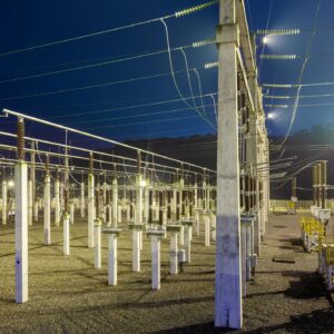 A nighttime view of a major electrical substation in Brazil, showcasing the complex network of high voltage insulators and wires.